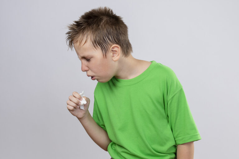 ill little boy in green t-shirt feeling unwell coughing standing over white background